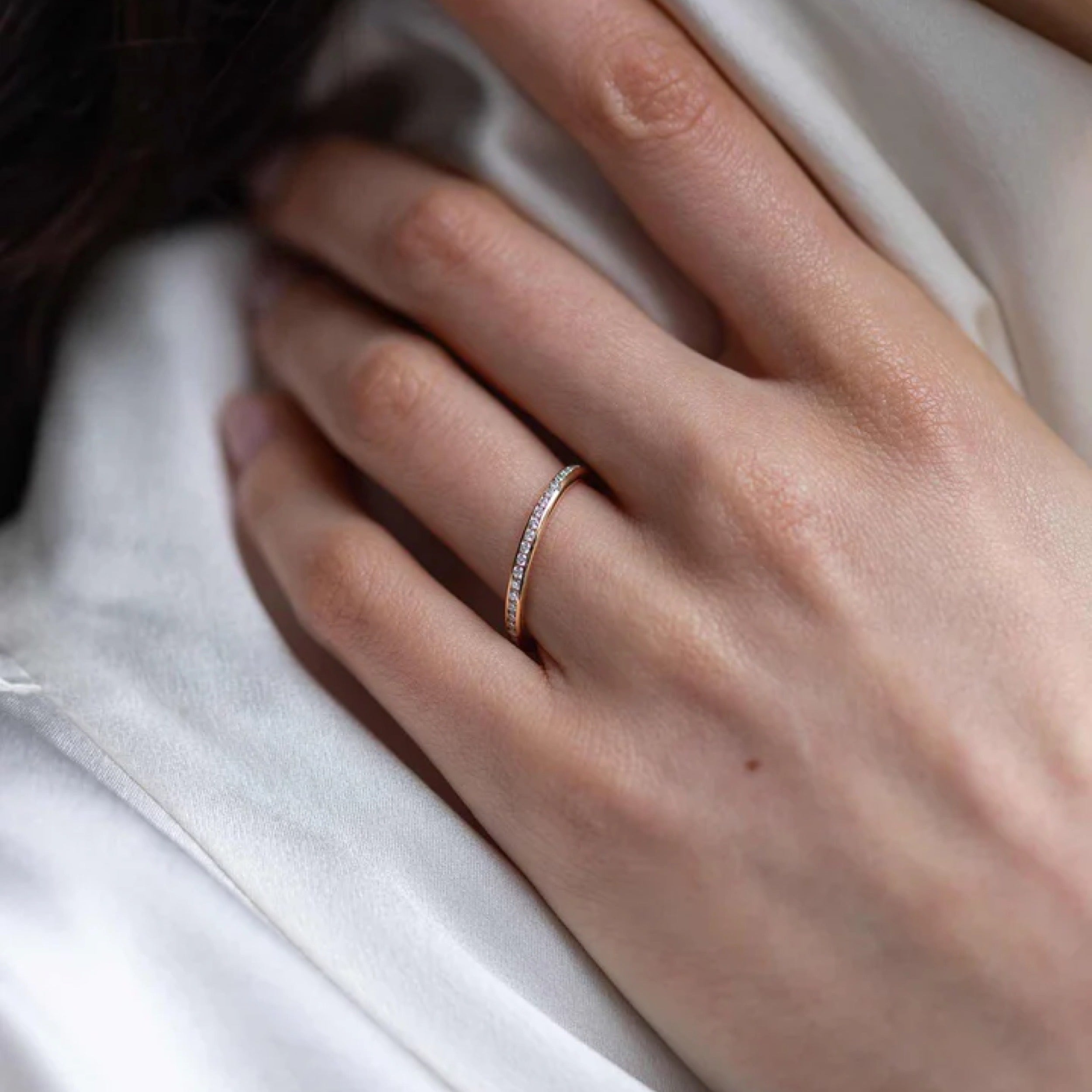 Elegant hand wearing a 0.35 TCW round cut diamond wedding band on a satin background.